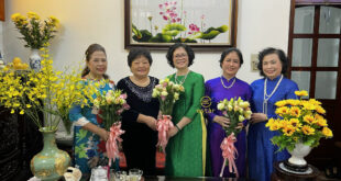 Tranh Thêu Hoa Sen Tranh thêu hoa sen nghệ thuật ESTAR treo trong phòng khách, phía trước là nhóm phụ nữ mặc áo dài chụp ảnh lưu niệm